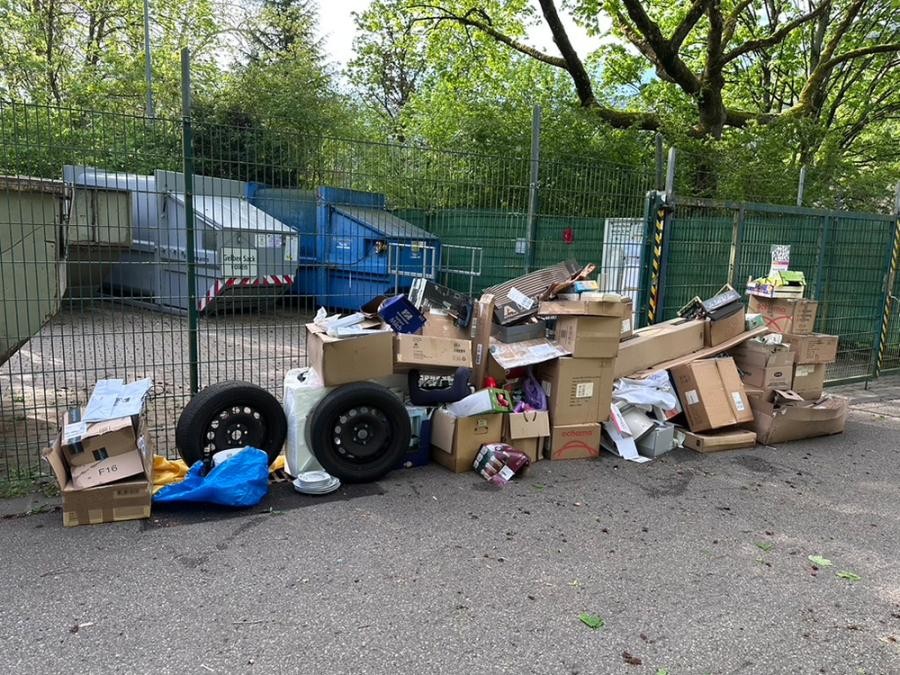 Am Recyclinghof Ziegelhausen wurden Kartons, Reifen und weiterer Abfall illegal vor dem Tor abgestellt. Das belastet die Umwelt und verursacht Kosten für alle Bürgerinnen und Bürger. (Foto: Stadt Heidelberg) Kartons, Reifen und weiterer Unrat liegen vor einem Metallzaunzaun, dahinter Müllcontainer.