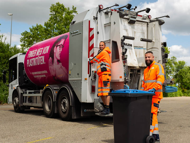 Zwei Müllwerker vor einem Abfallfahrzeug.