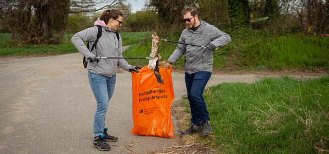 Zwei Menschen sammeln Abfall mit einer Greifzange